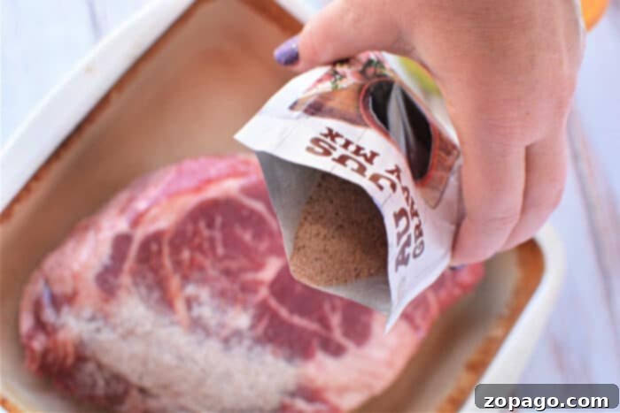 Slow Cooker Mississippi Pot Roast 4 Hand pouring dry gravy mix onto raw steak in a baking dish, this setup hints at the beginnings of a delightful Mississippi Pot Roast recipe.