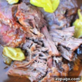 Slow Cooker Mississippi Pot Roast 7 Close-up of juicy, shredded beef with peppers in rich broth, reminiscent of a savory Mississippi Pot Roast.
