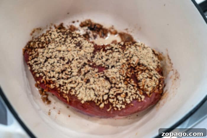 Slow-Cooked Pot Roast with Caramelized Onions 4 A roast piece of meat in a pot, topped with a mix of spices, herbs, and caramelized onions, ready to be cooked.