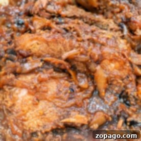 A close-up of braised beef brisket with caramelized onions in a rich, savory roast sauce.