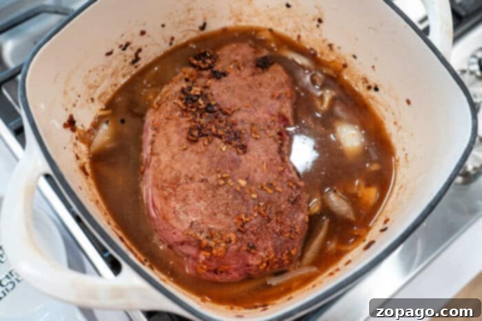 Slow-Cooked Pot Roast with Caramelized Onions 7 Savory roast beef simmered gently in a pot with caramelized onions and hearty broth on the stove.
