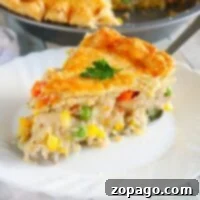 A slice of golden-crusted chicken pot pie, made from a simple recipe, sits invitingly on a white plate, brimming with vegetables.