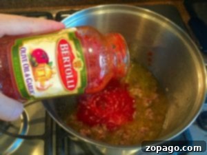 Streamlined Spaghetti Supper 6 A hand pours Bertolli olive oil and garlic sauce into a pot on the stovetop, setting the stage for a delicious one-pot spaghetti dish.