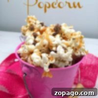 A pink pail brimming with peanut butter chocolate popcorn, sprinkled with delectable chocolate pieces, sits beside a soft pink fabric. Above it, the text reads: Peanut Butter Popcorn.