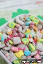 A colorful cereal mix with marshmallows, sprinkles, and square cereal pieces in a white bowl is reminiscent of a playful twist on a classic Peanut Butter Muddy Buddies recipe.