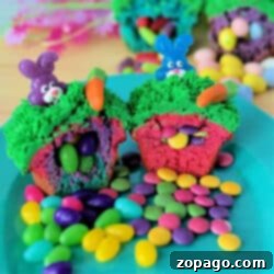 Colorful Surprise Inside Cupcakes with green frosting, topped with plastic bunnies and carrots, cut open to reveal candy treasures inside, displayed on a turquoise plate surrounded by scattered candies.