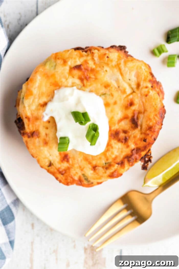 Crispy Cheesy Potato Cakes 8 A cheesy potato pancake topped with sour cream and chopped green onions, served with lime wedges on a white plate, reminiscent of fried mashed potatoes with cheese.