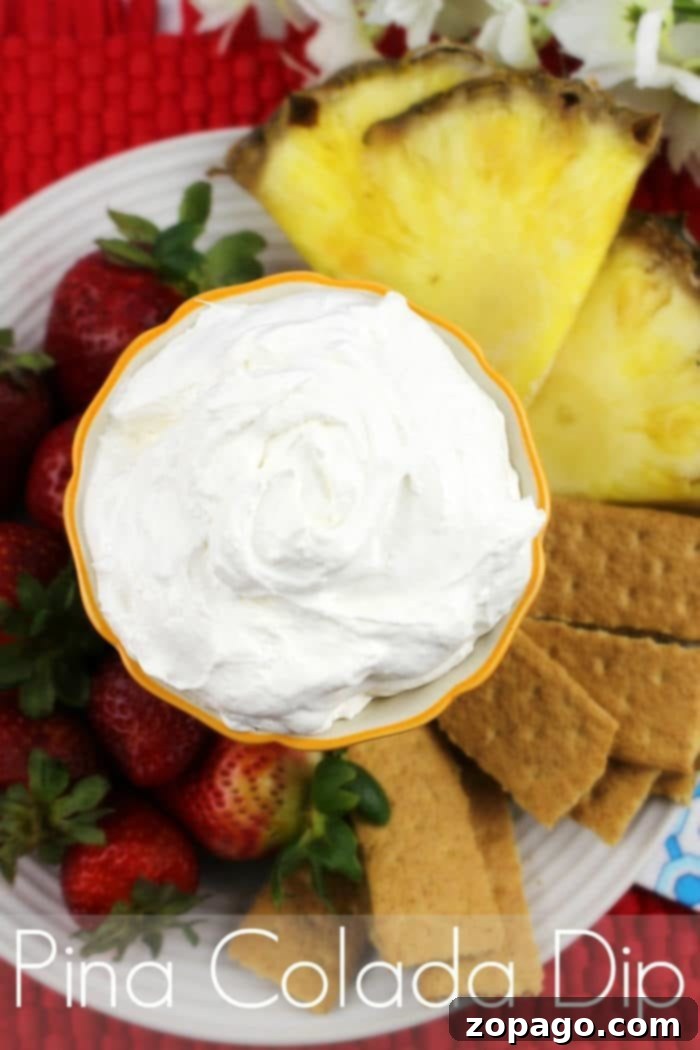 Creamy Pineapple Delight Dip 2 A vibrant bowl of creamy Pina Colada dip, generously garnished with toasted coconut flakes and fresh pineapple chunks, is surrounded by an assortment of colorful dippers including sliced strawberries, crisp graham crackers, and vanilla wafers, all artfully arranged on a rustic wooden platter for a perfect party spread.