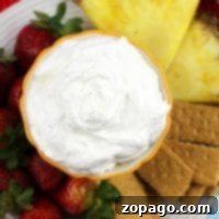 A bowl of creamy Pina Colada dip sits enticingly surrounded by sliced pineapple, strawberries, and graham crackers on a plate.