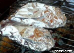 Two foil-wrapped food items, possibly grilled stuffed peppers, cook on a grill over hot coals.