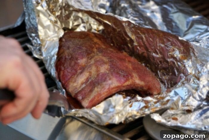 Checking the progress of our barbecue ribs recipe, these grilled ribs wrapped in foil are sizzling perfectly on the grill. Grilled ribs wrapped in foil, sizzling on the barbecue, showcasing the slow cooking process for tender results.