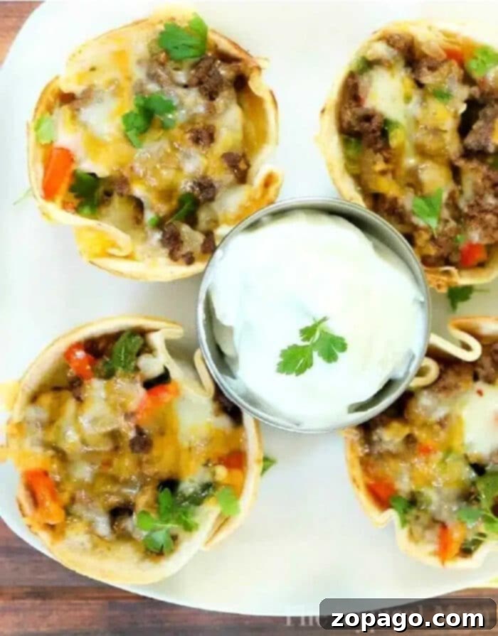 Fajita Bites 4 Steak fajita cups with ground beef, cheese, and veggies, served with a side of sour cream and garnished with fresh cilantro.