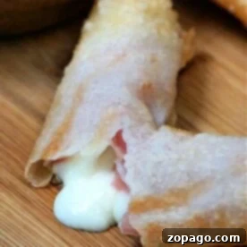 Crispy Ham and Cheese Egg Rolls 6 A close-up of a crispy air fryer ham and cheese egg roll on a wooden surface, with melted cheese oozing out from a break in the pastry.