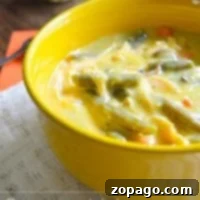 A yellow bowl of crockpot creamy chicken soup with vegetables sits elegantly on a lace tablecloth.