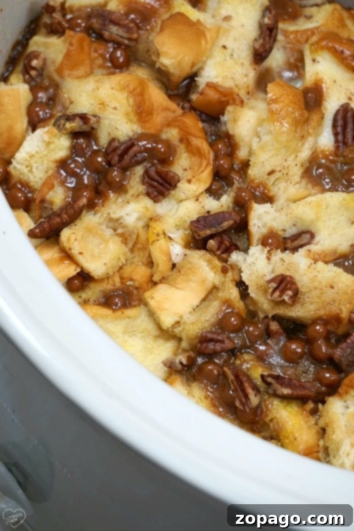 Caramel pecan crockpot french toast casserole is insane!! It's SO easy to make and a perfect brunch or Christmas breakfast!! Slow cooker style! A close-up of a steaming hot caramel pecan Crockpot French toast casserole, garnished with a sprinkle of powdered sugar and fresh berries, ready to be served for a festive breakfast or dessert.