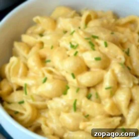 A bowl of creamy Instant Pot macaroni and cheese garnished with chopped chives rests on a blue surface.