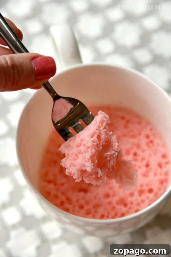 Angel's Delight in a Mug 3 A vibrant strawberry cake in a mug, showcasing its colorful topping and soft texture.