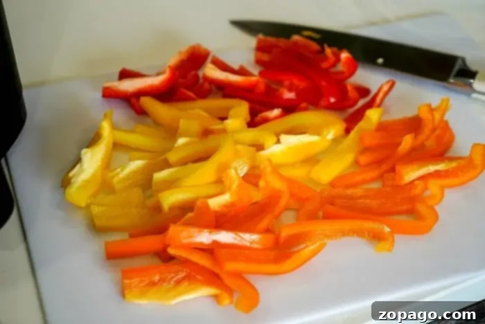 Effortless Bell Pepper Blanching 3 Sliced red, yellow, and orange bell peppers are arranged on a white cutting board, ready for the next step in learning how to blanch bell peppers. A knife is placed nearby on the board.