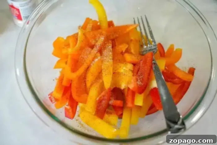 Effortless Bell Pepper Blanching 7 A glass bowl brimming with vibrant, sliced red, yellow, and orange bell peppers is artfully seasoned. If you're curious about prepping them further, learning how to blanch bell peppers can enhance their texture. A fork and spoon are nestled inside the bowl for easy serving.