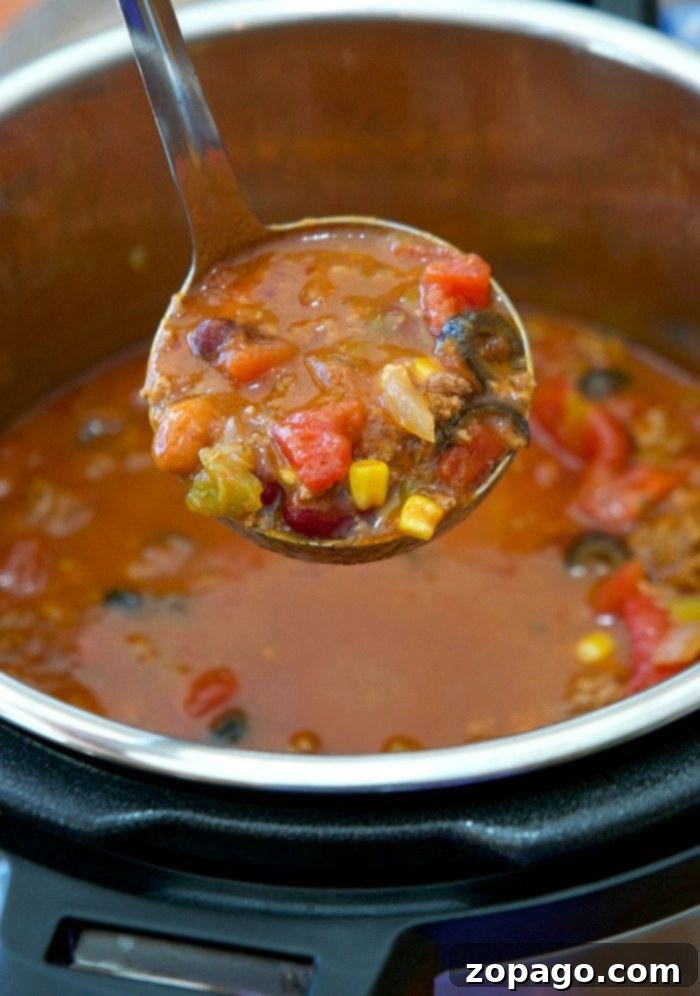 Instant Pot taco soup recipe is perfect year round and packed with flavor. Just 6 minutes in your pressure cooker topped with sour cream and a side of chips or a roll and it's the perfect family meal! Need a warm soup during the Winter or just love anything tacos, give this a whirl. #instantpot #pressurecooker #taco #soup #thetypicalmom #instantpotrecipes A ladle serving a hearty taco soup with beans, tomatoes, corn, and meat from the pot—a simple take on an easy Instant Pot taco soup recipe.