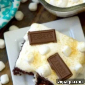 A delicious s'mores poke cake, adorned with marshmallows and Hershey bars, sits elegantly on a white plate.