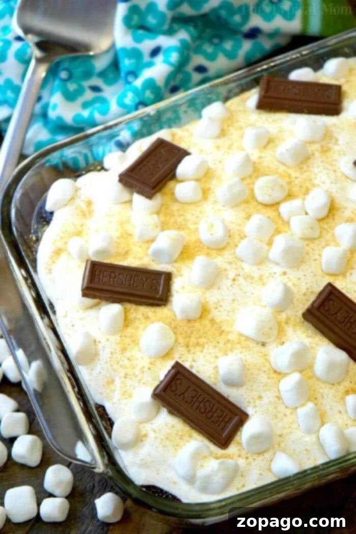 A perfect slice of S'mores Poke Cake revealing its moist chocolate interior infused with chocolate sauce, crowned with soft toasted marshmallows and crispy graham cracker crumbs. An easy and irresistible dessert for any S'mores enthusiast. Slice of S'mores Poke Cake on a plate with gooey marshmallow and chocolate