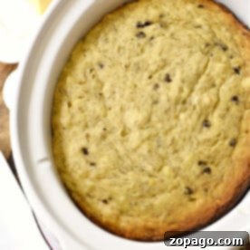 A baked dish in a white casserole, reminiscent of slow cooker banana bread, with a block of butter on the side, rests invitingly on a wooden table.