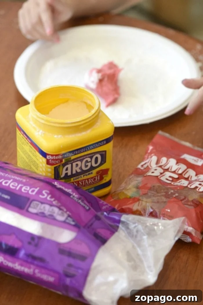 Kid-Friendly Edible Gummy Bear Slime Recipe Child's hands playing with a large blob of pink edible gummy bear slime on a paper plate.