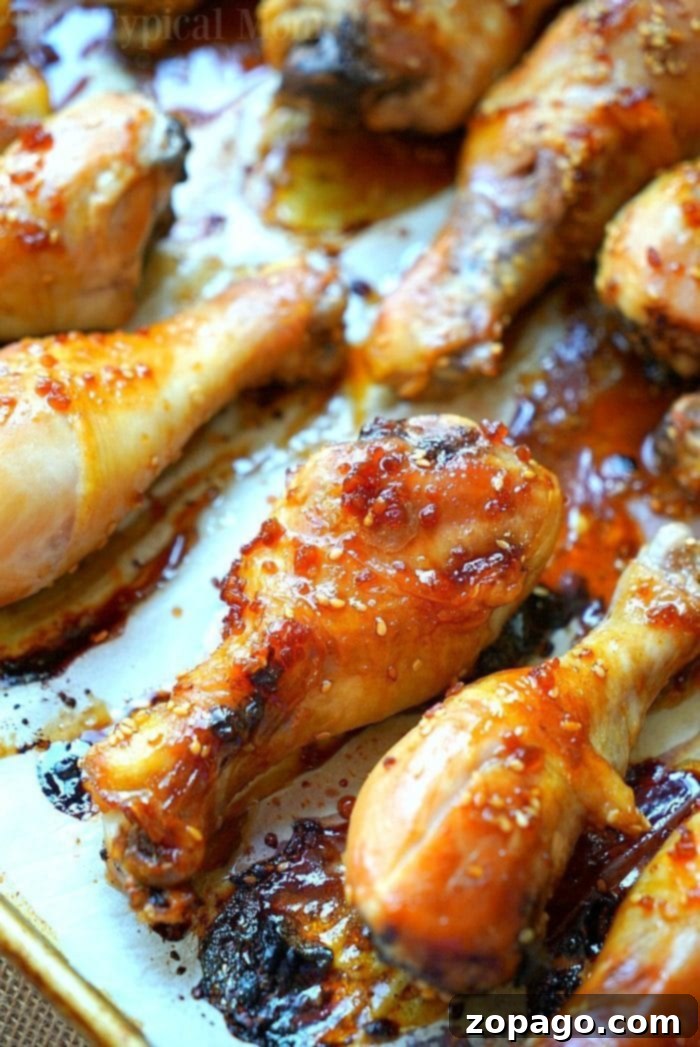 Baked Teriyaki Chicken Drumsticks with Homemade Sweet and Spicy Sauce Close-up of baked teriyaki chicken drumsticks glazed with a sticky, golden-brown sauce, arranged on a baking tray with visible sesame seeds and caramelized edges.