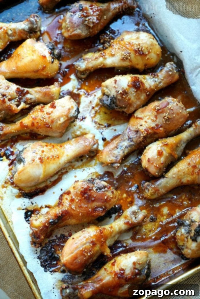 Baked Teriyaki Chicken Drumsticks with Homemade Sweet and Spicy Sauce Succulent teriyaki chicken drumsticks with a glistening sauce, garnished with sesame seeds, on a parchment-lined baking sheet.