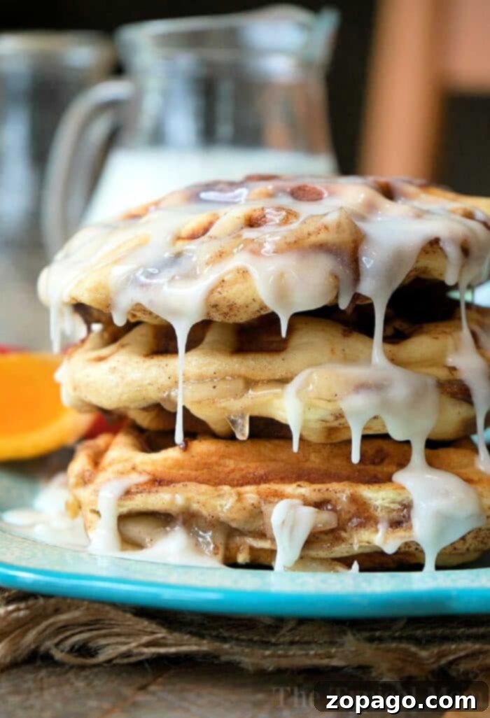 Apple Pie Stuffed Cinnamon Roll Waffles: The Ultimate Breakfast or Dessert Stack of golden-brown apple pie stuffed cinnamon roll waffles drizzled with icing on a blue plate, with a pitcher of milk in the background. Perfect for breakfast or dessert.