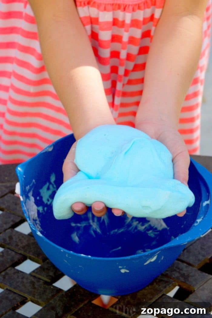 How to make fluffy slime with just 3 ingredients and no borax! Fun kid safe slime recipe that feels soft and you can make any color you like. Simple fun! Child's hands mixing white glue and shaving cream in a bowl, preparing to make fluffy slime.