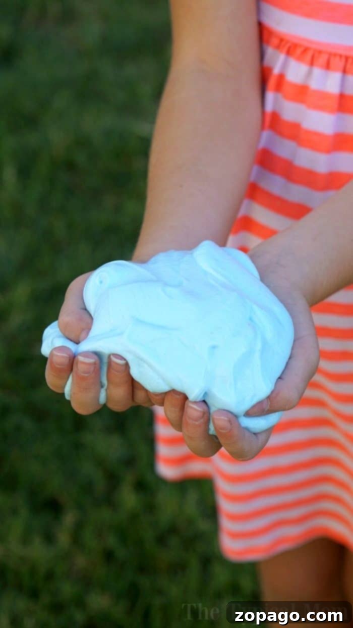 How to make fluffy slime with just 3 ingredients and no borax! Fun kid safe slime recipe that feels soft and you can make any color you like. Simple fun! Child's hands kneading pink fluffy slime, showcasing its soft, stretchy texture.