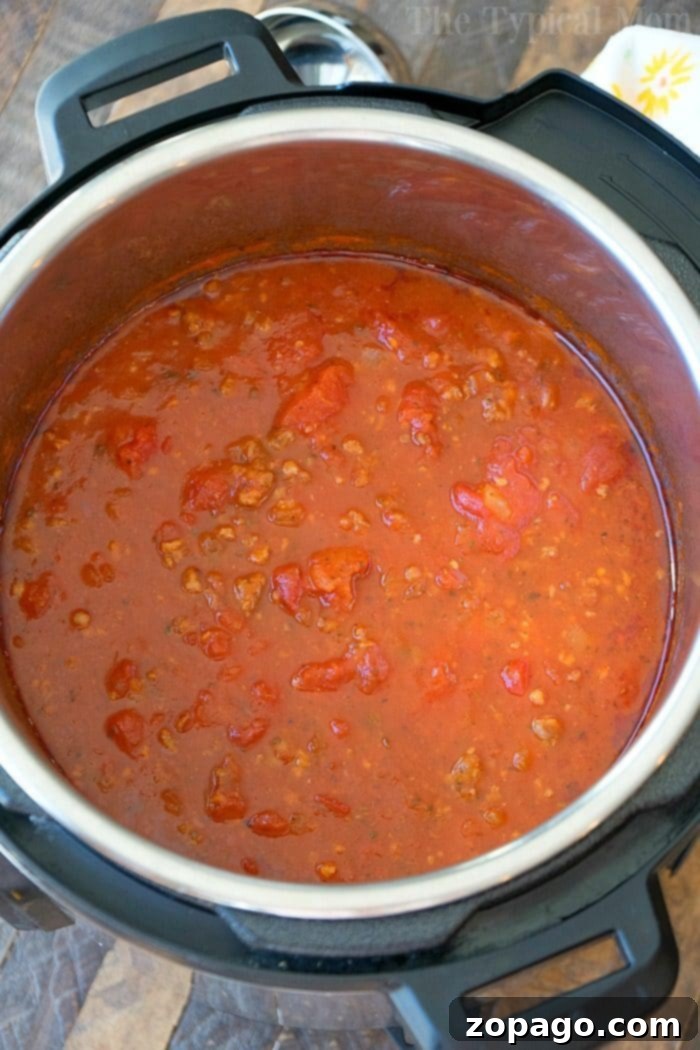 Homemade Instant Pot spaghetti sauce recipe! All you need are a few cans of this and a roll of that to make the most flavorful sauce ever. I literally threw this together in 10 minutes and 20 minutes later it was done. Way better than any jarred sauce. #instantpotrecipes #instantpot #pressurecooker #homemade #spaghetti #sauce #thetypicalmom An open Instant Pot reveals a hearty sauce simmering with tomatoes and ground meat, reminiscent of a robust spaghetti sauce.