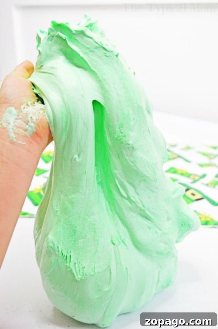 Easy Borax-Free Fluffy Slime with Shaving Cream for Kids' Crafts and Parties Child's hands stretching vibrant green fluffy slime made with shaving cream, perfect for a borax-free and kid-safe St. Patrick's Day activity.