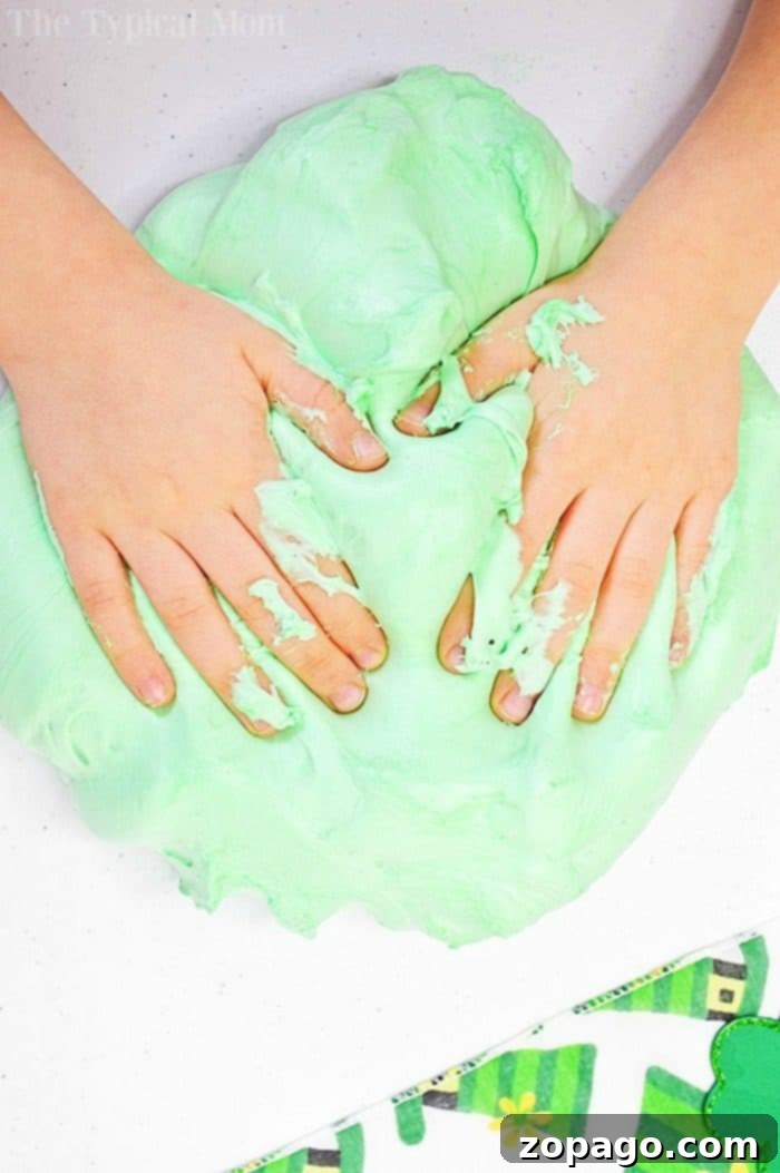 Making Fluffy Blue Shaving Cream Slime for Kids: A Borax-Free Recipe Close-up of a child's hands gently playing with fluffy blue shaving cream slime, demonstrating its soft and pliable texture.