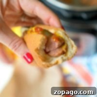 A hand holds a bitten hot dog with mustard and ketchup, the vibrant red nails adding a pop of color. Perfectly cooked using an Instant Pot, this hot dog promises both convenience and flavor in every bite.