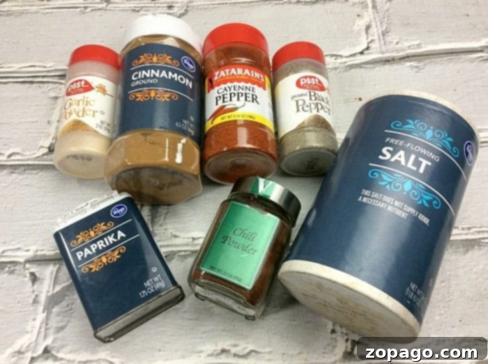 Ultimate Air Fryer Wings 3 A collection of spice containers on a white brick surface, perfect for an air fryer wings recipe, includes garlic powder, ground cinnamon, cayenne pepper, black pepper, paprika, chili powder, and salt. Each container showcases distinct branding and labels.