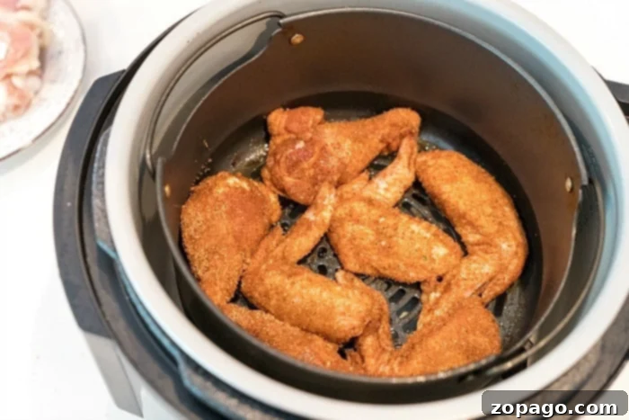 Ninja Foodi chicken wings. In an enticing air fryer wings recipe, chicken wings seasoned with spices rest in the air fryer basket, ready to be cooked to perfection. The air fryer stands proudly on the kitchen counter, with a glimpse of a plate holding raw chicken visible in the background.