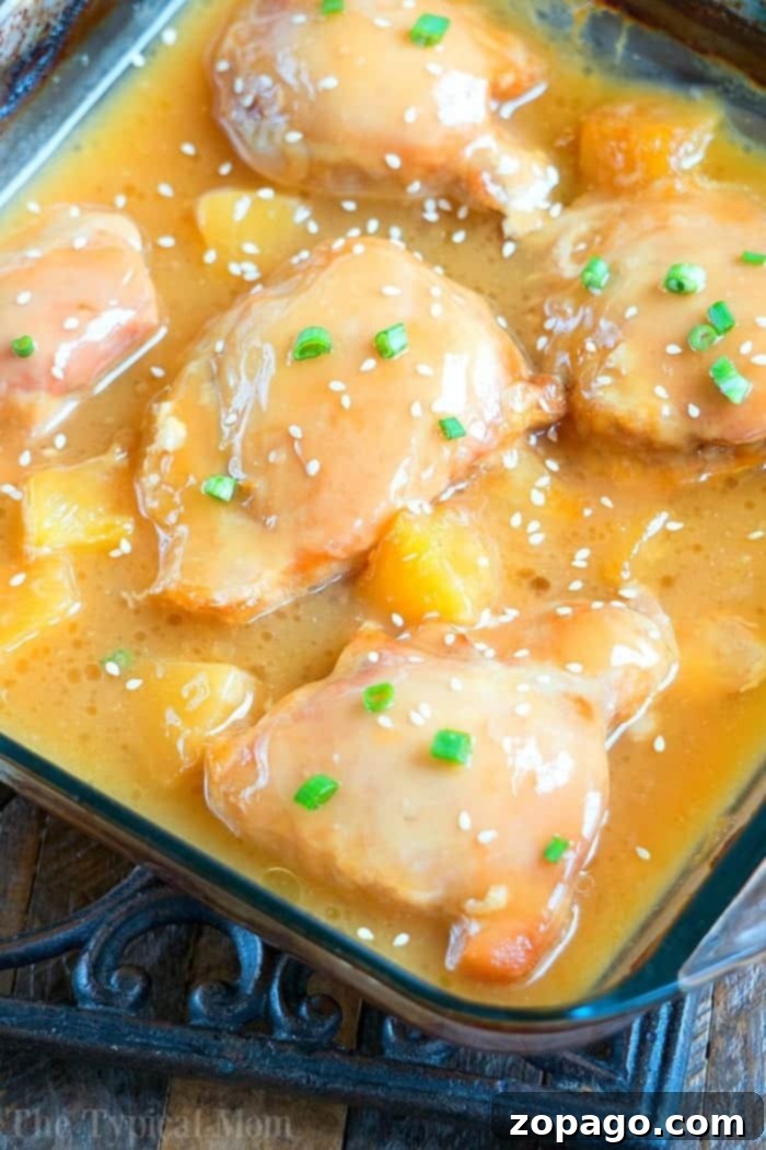 An easy pineapple chicken recipe using succulent chicken thighs, baked to perfection with a sweet and savory glaze, enhanced by tender pineapple pieces. Close up of a piece of easy pineapple chicken with pineapple chunks and a sweet glaze.