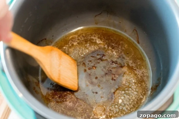 A wooden spatula gently stirs browning butter in a pot, the aroma mingling with the richness of pressure cooker short ribs. The butter bubbles, forming a caramelized layer at the bottom, enhancing the flavors of this delicious dish.