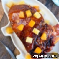Effortless Crockpot Ham 2 A glazed ham with pineapple chunks sits invitingly on a white platter, reminiscent of a delicious crockpot ham recipe, all elegantly arranged on a wooden table adorned with a blue napkin.