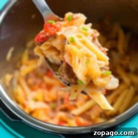 Hearty Instant Pot Sausage and Cabbage 3 A spoonful of pasta with ground meat and vegetables, reminiscent of a hearty pressure cooker sausage and cabbage dish, held above a pot of pasta.