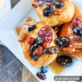 Sticky Bun recipe with Crescent Rolls topped with pecans, raisins, and dried cranberries served on a white plate.