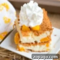 A slice of delightful peach angel food cake topped with whipped cream sits gracefully on a white square plate. The light, fluffy cake reveals juicy peach chunks. A patterned cloth accentuates the scene alongside a baking dish, creating an inviting and warm presentation.