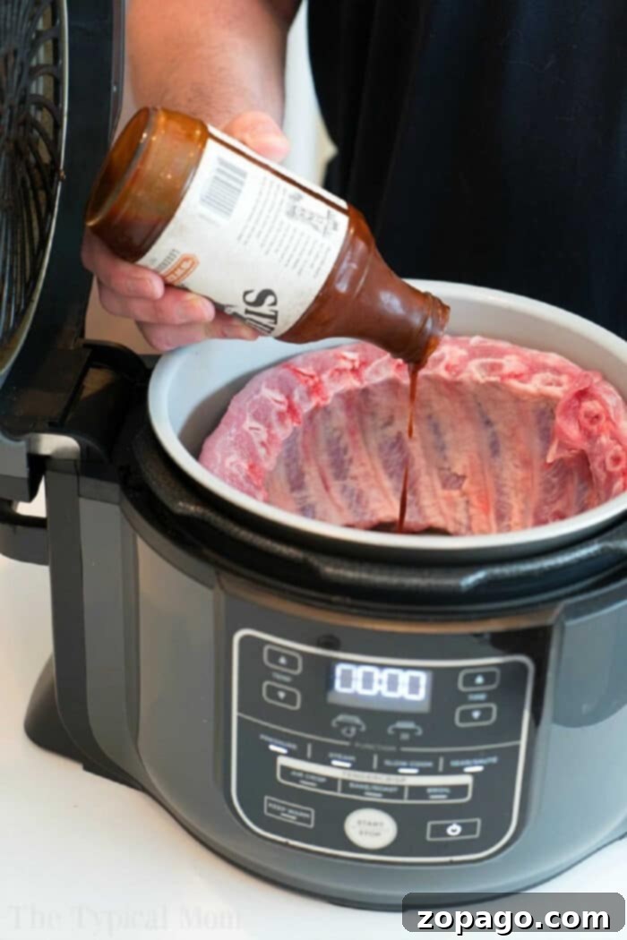 Prepare mouthwatering Ninja Foodi ribs: tender pork ribs with a crispy barbecue glaze, cooked using both pressure cooker and air fryer functions. Person pouring barbecue sauce onto raw ribs in a Ninja Foodi, getting the Ninja Foodi ribs ready to be cooked to tender perfection.