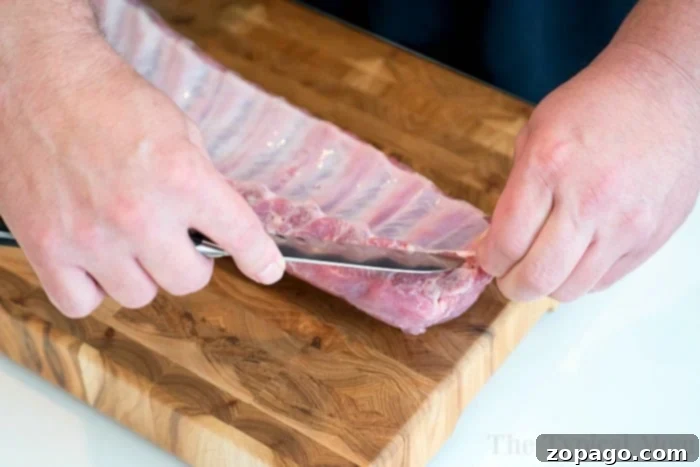Removing the rib membrane is crucial for incredibly tender, fall-off-the-bone Ninja Foodi ribs, perfectly prepped for pressure cooking and air frying. Close-up of a hand skillfully removing the membrane from a rack of ribs, a critical step for tender Ninja Foodi ribs.