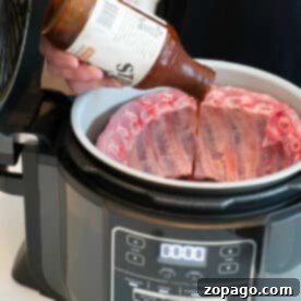 Person pouring barbecue sauce onto raw ribs in a Ninja Foodi, getting the Ninja Foodi ribs ready to be cooked to tender perfection.