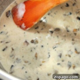A wooden spoon stirs a pot filled with rich, homemade cream of mushroom soup, blending warmth and comfort in every swirl.