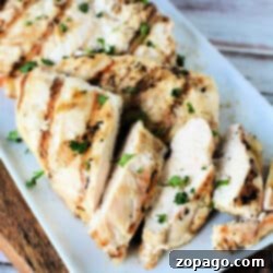 From Freezer to Fabulous: Air Fryer Chicken Breast 4 A plate of grilled chicken breast slices garnished with chopped parsley. The chicken, originally cooked as frozen chicken breast in an air fryer, has visible grill marks and the slices are arranged neatly on a rectangular white plate. The background includes a wooden surface.